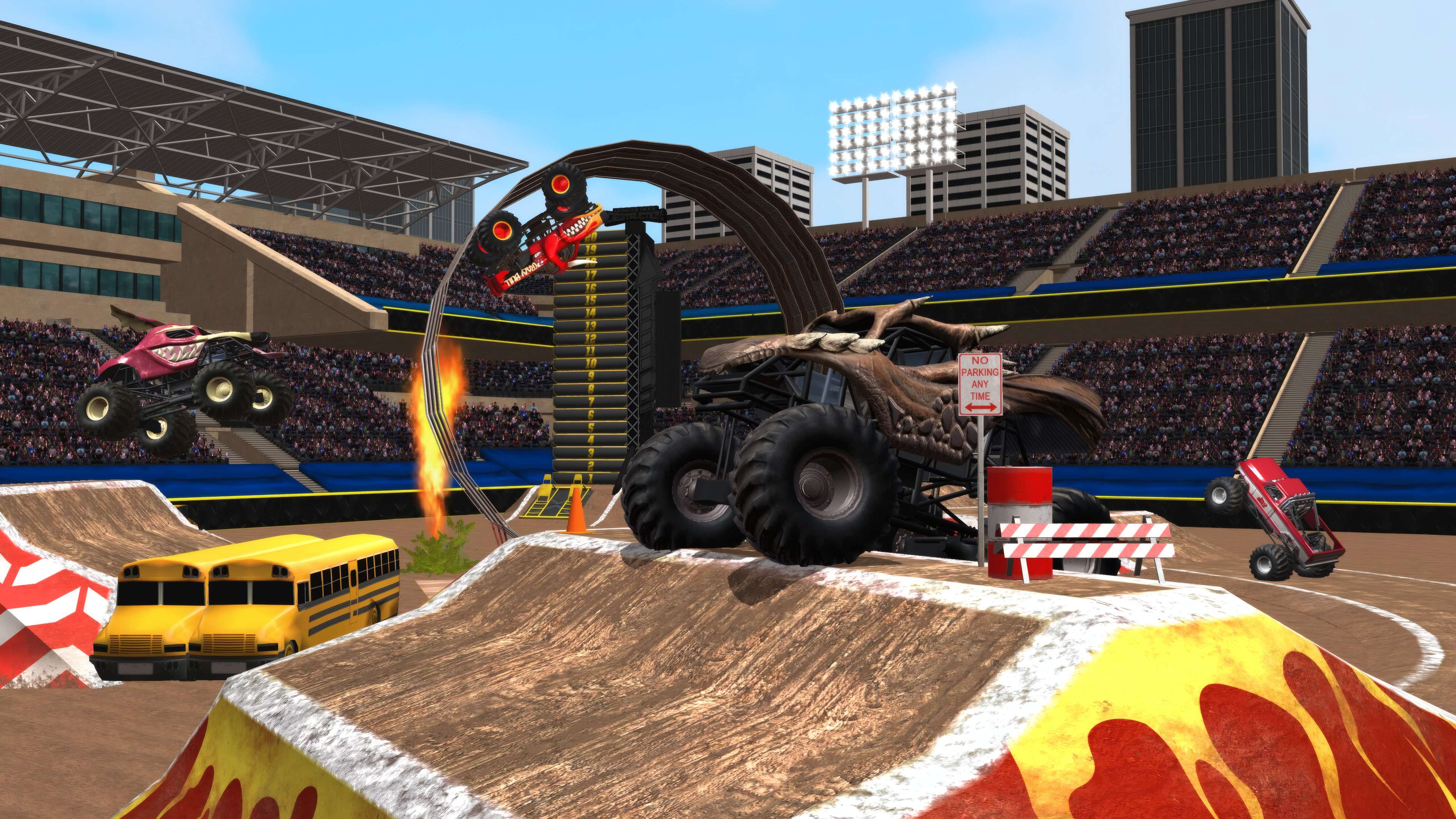 Monster trucks jumping through a ring of fire in a dirt stadium